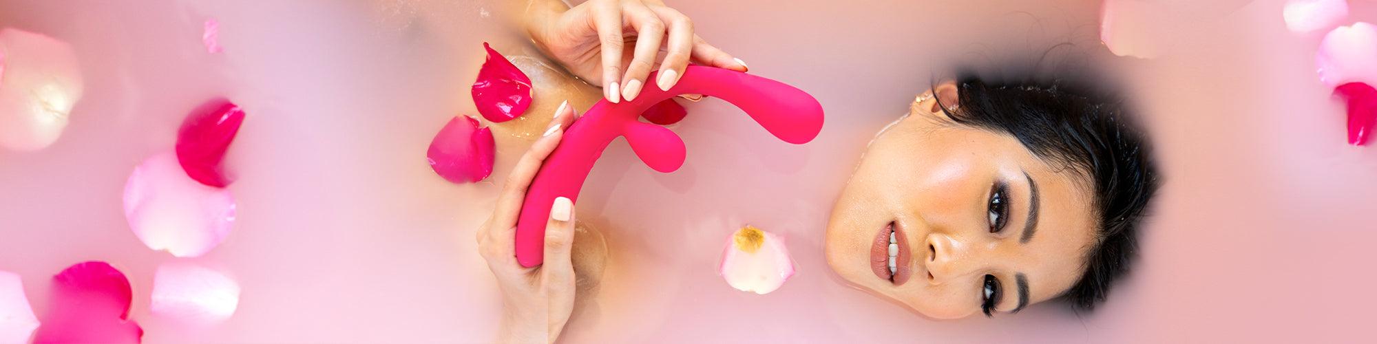 Woman in a milk bath with rose petals, holding a pink luxury massager by JIMMYJANE