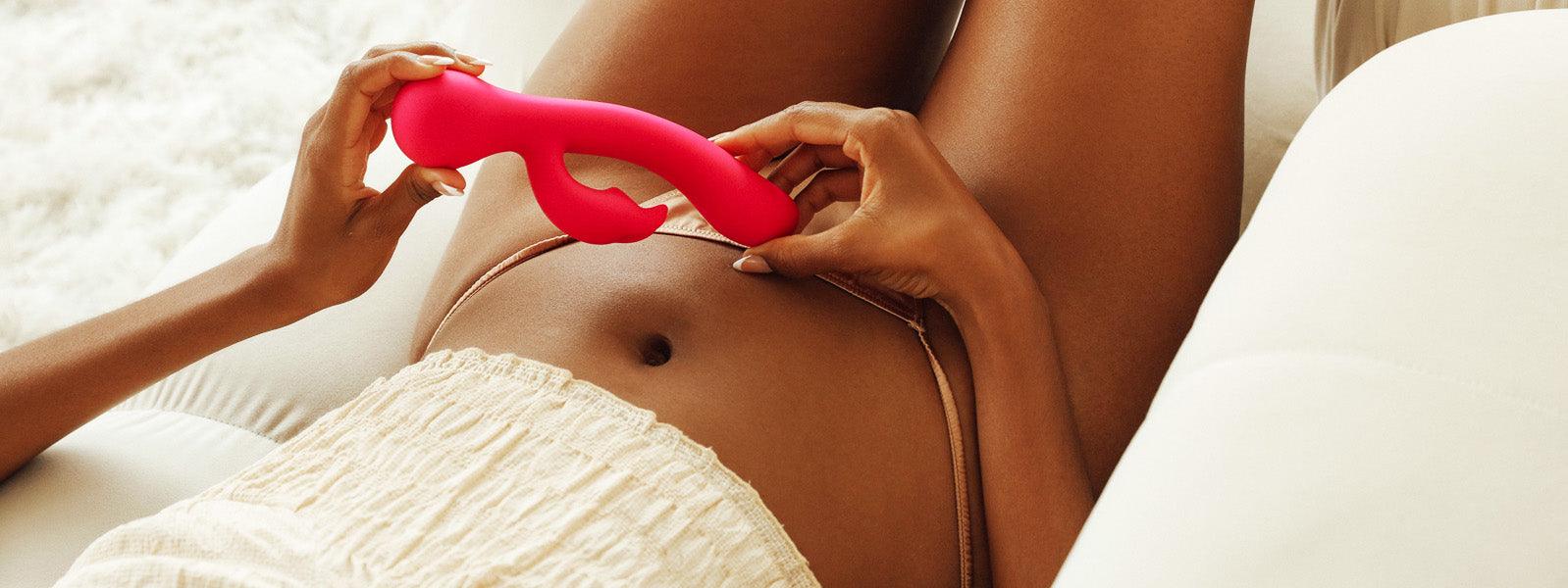 Person holding luxury pink wellness massager on abdomen, relaxing on cream sofa