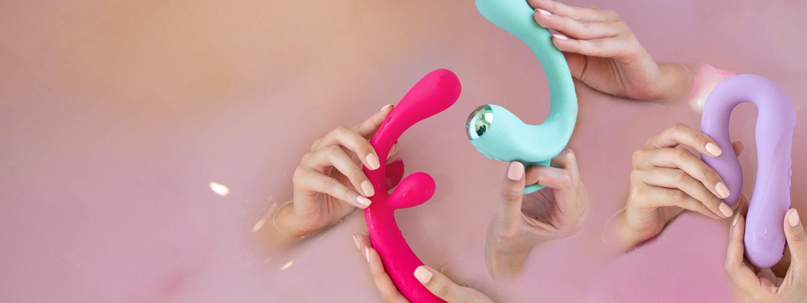 Hands holding colorful luxury personal massagers in pink, mint, and lavender on soft background