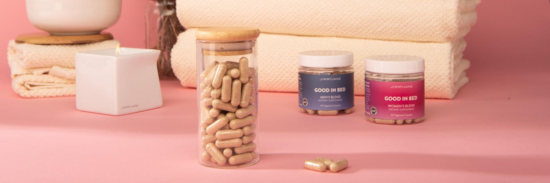 JIMMYJANE Good In Bed dietary supplements jars and capsules on pink spa setting with towels and candle.