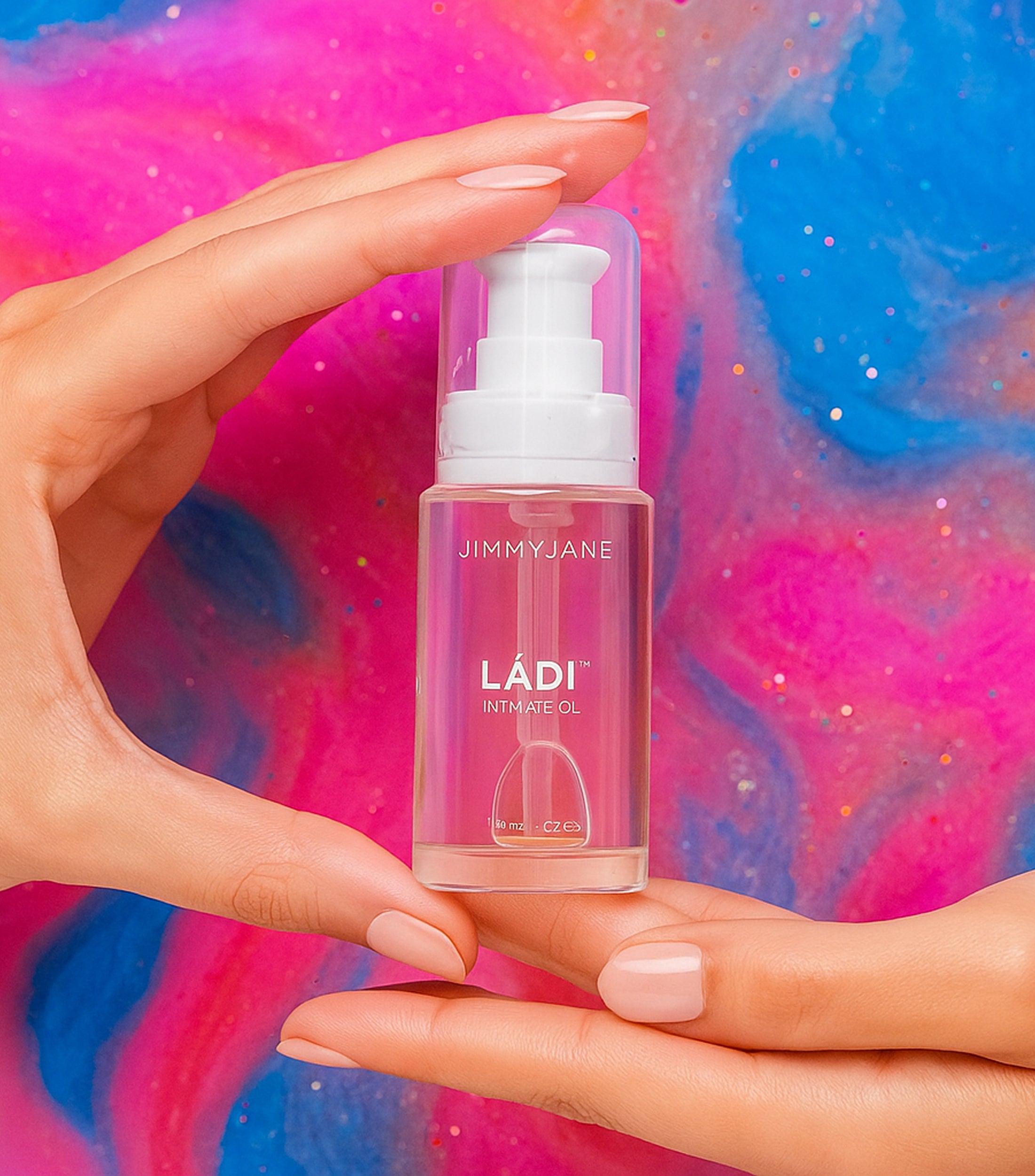 Hand holding a bottle of Jimmyjane Ladi intimate oil against a colorful abstract background