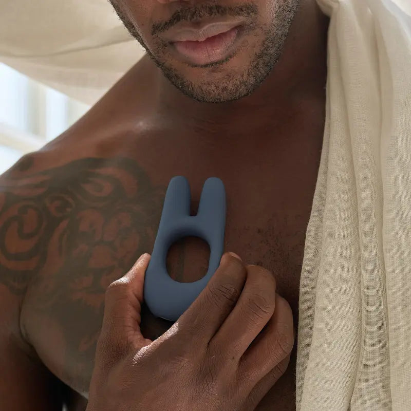 Man holding a blue luxury wellness device by JIMMYJANE near chest with lion tattoo and towel
