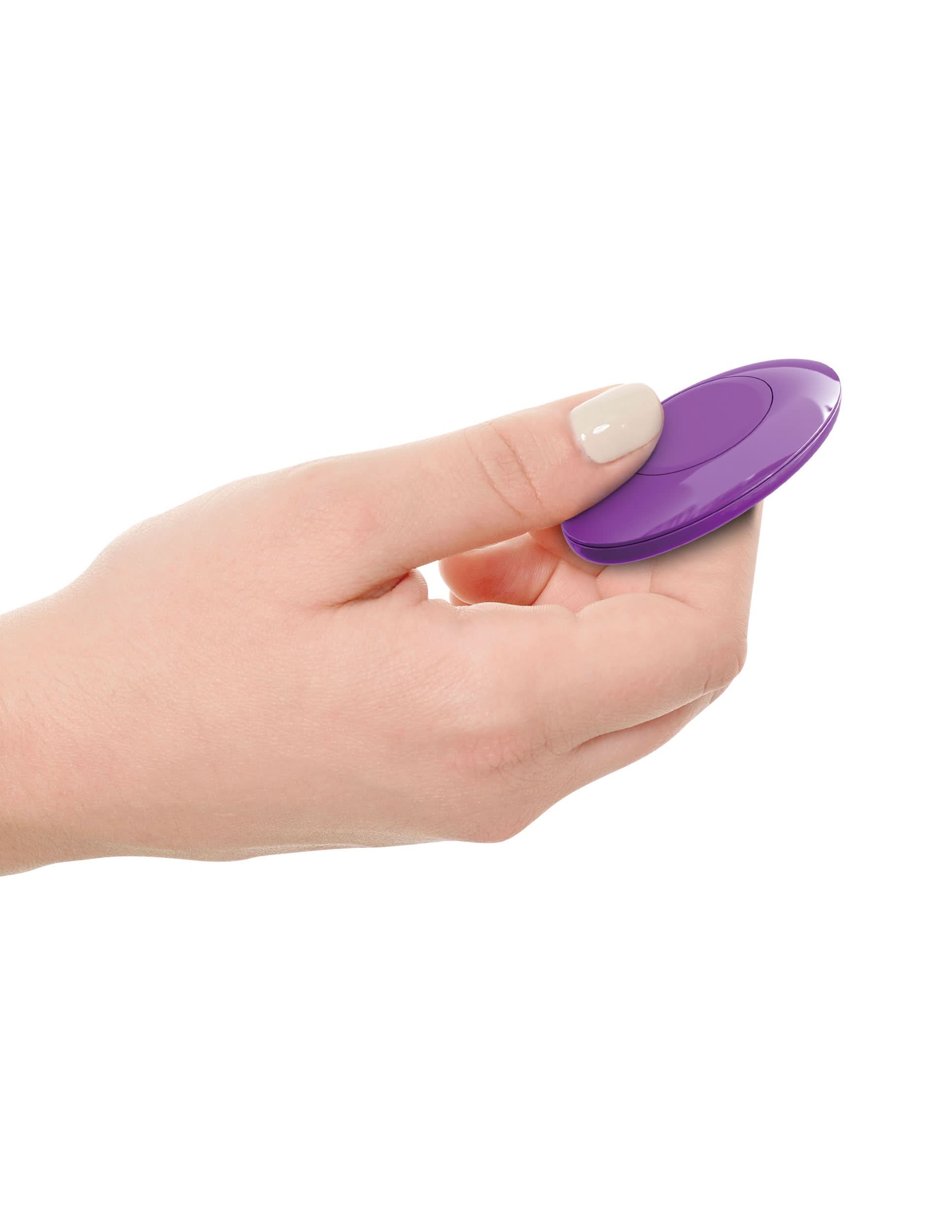 A hand holds the 3Some Pipedream® Wall Banger Plug, a small, round, purple massager with a smooth surface, against a white background.