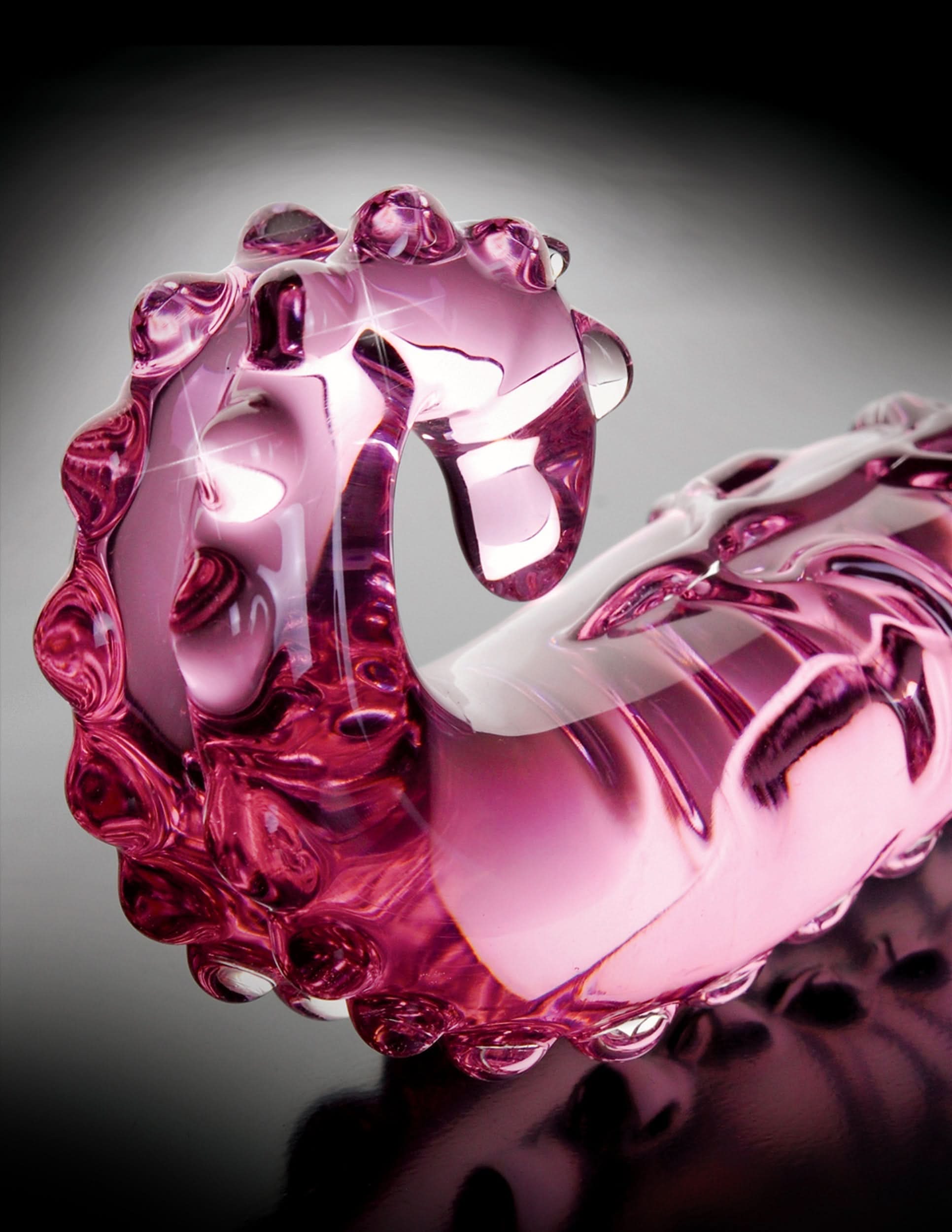 The Icicles® No. 24 by Icicles® is a glossy pink, hand-blown glass sculpture featuring a curved, bumpy texture, shown resting on a reflective surface.