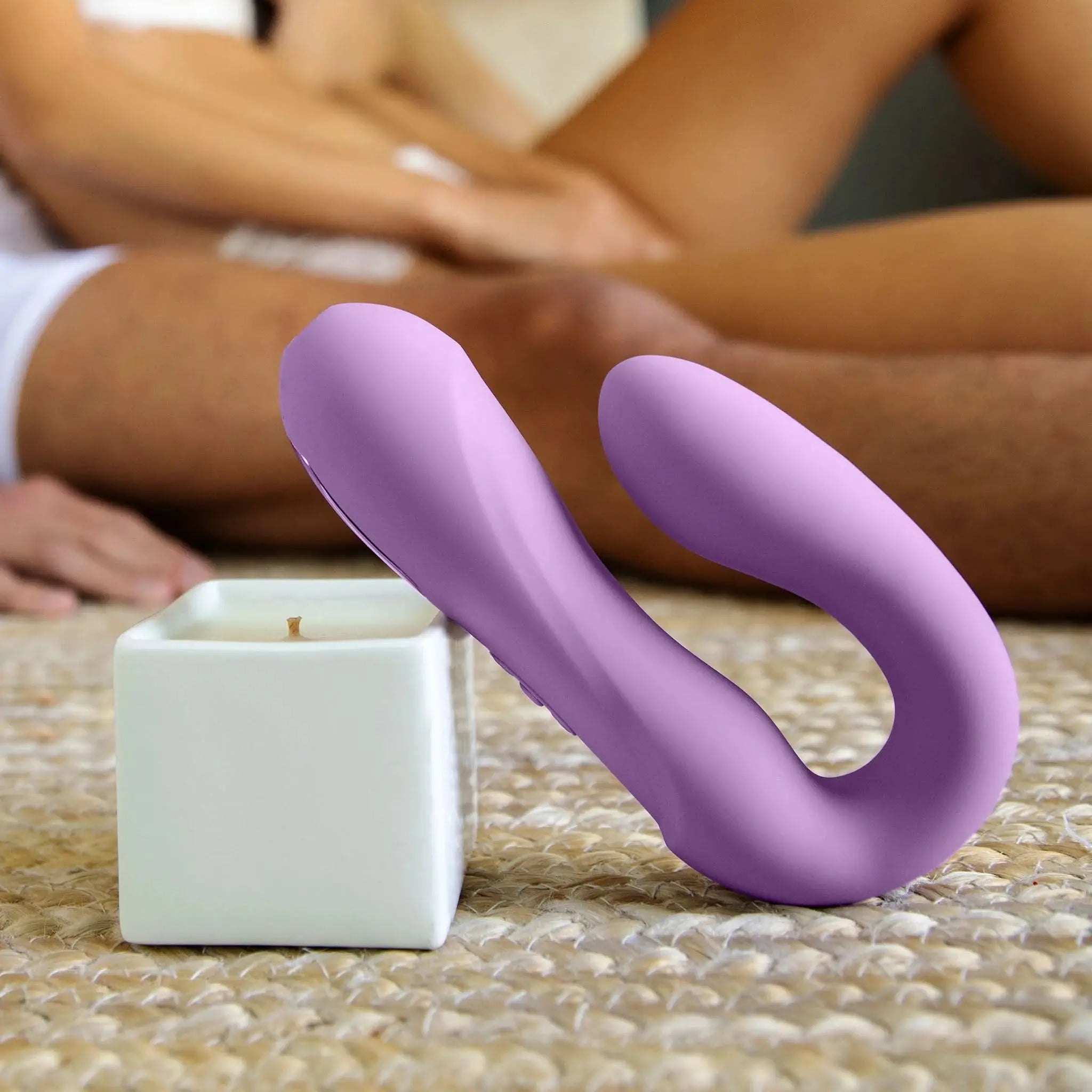 Purple luxury wellness device from JIMMYJANE near candle on woven rug, couple blurred in background