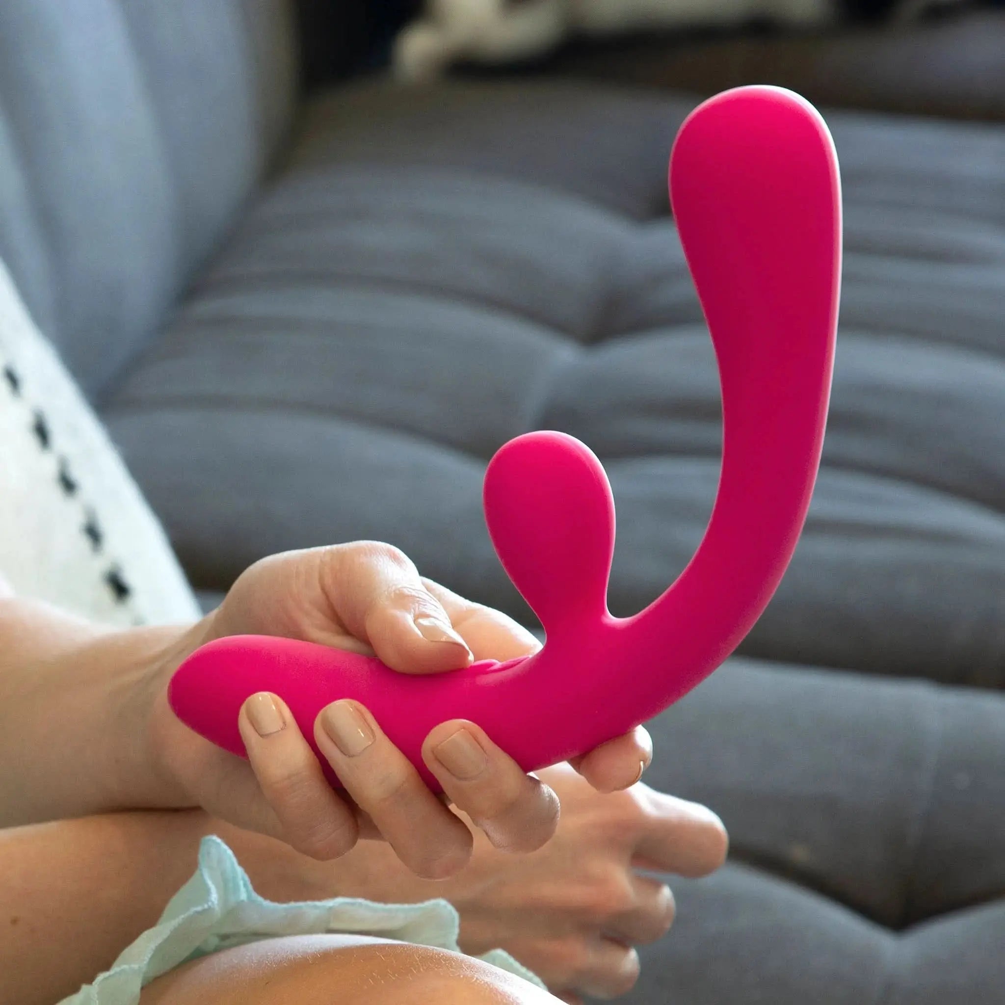 Hand holding a pink luxury JIMMYJANE silicone massager on a gray sofa