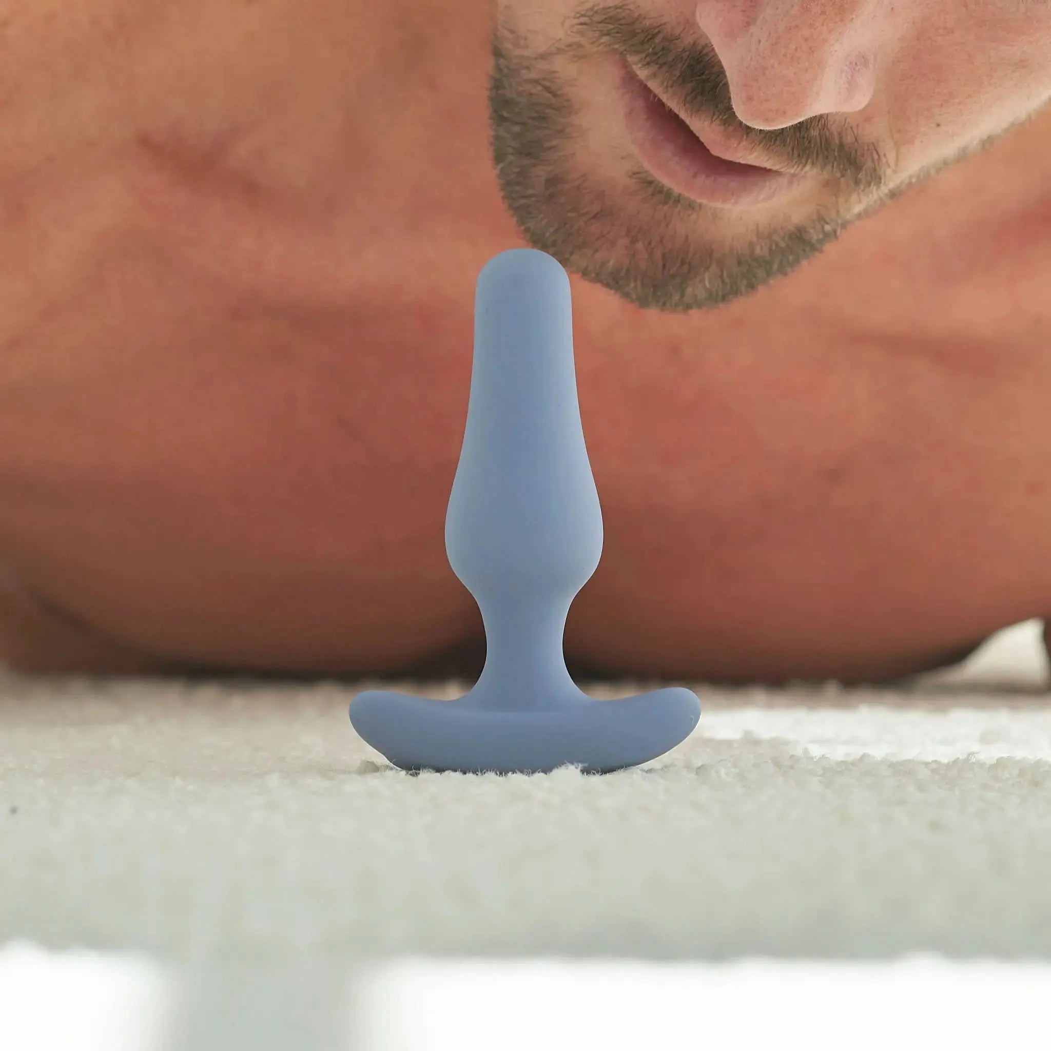 Man lying on carpet near blue silicone plug from JIMMYJANE luxury adult toy collection.
