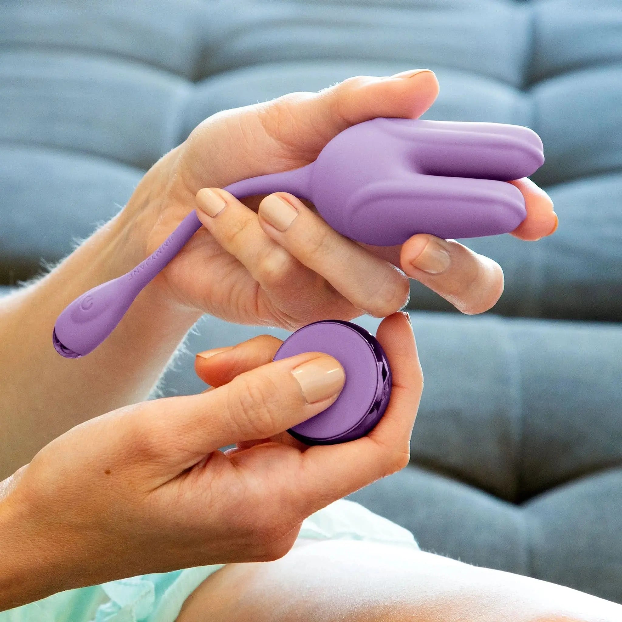 Person holding purple JIMMYJANE luxury wellness device and remote on a sofa