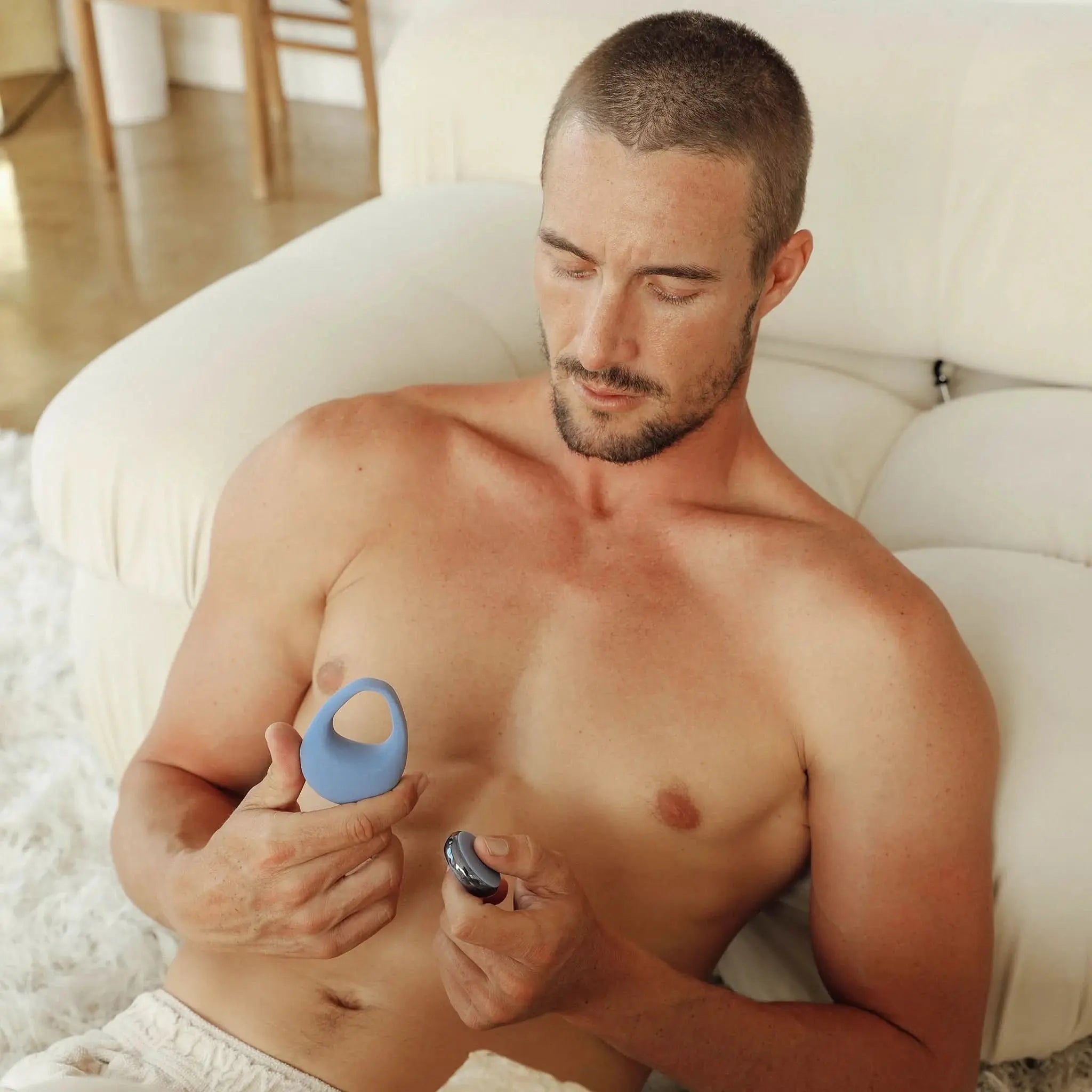 Man relaxing on sofa holding blue JIMMYJANE luxury wellness ring and remote control