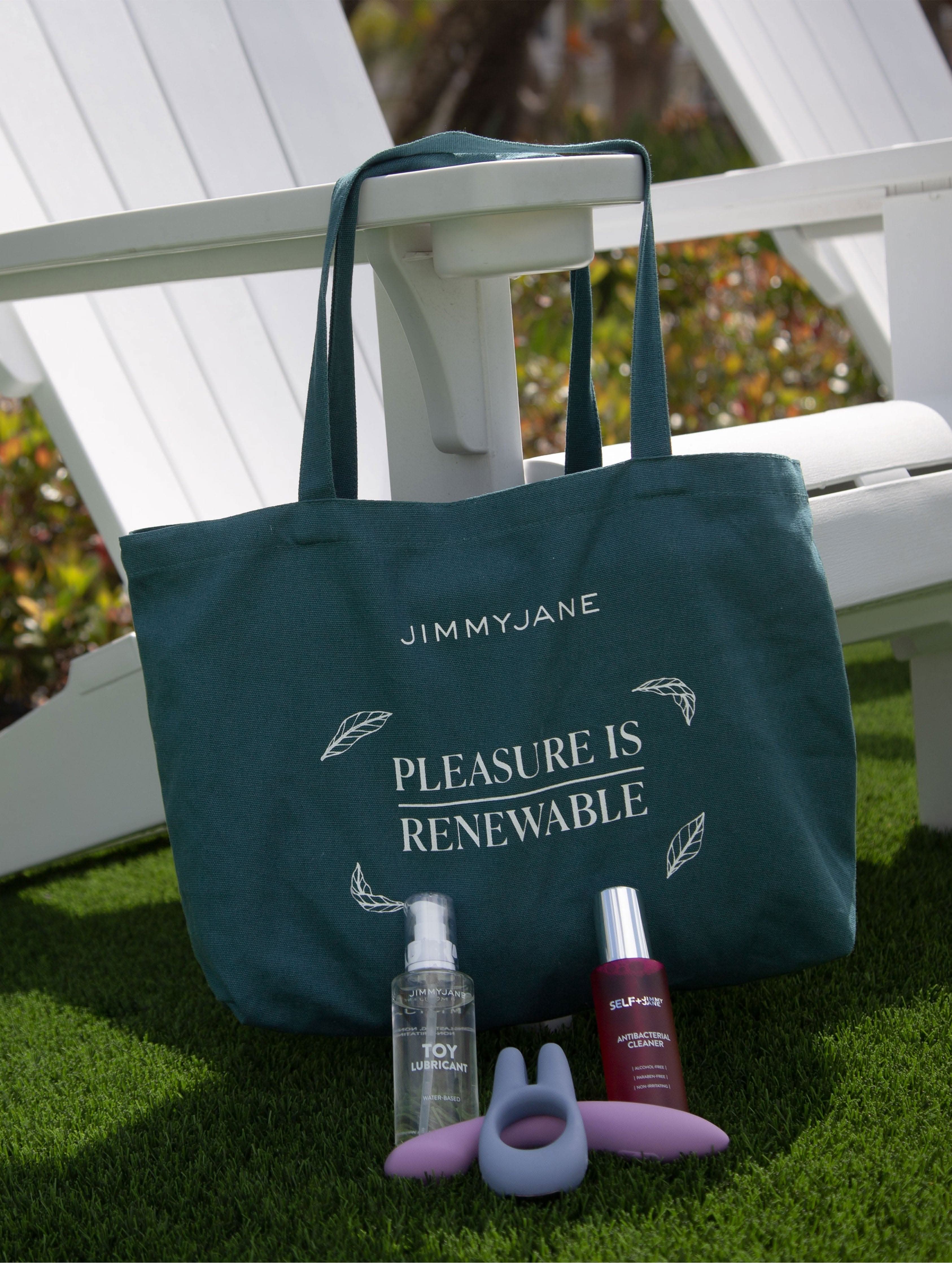 The JIMMYJANE® Reusable Pleasure Tote features an eco-friendly bag with “Pleasure is Renewable” text and includes a lubricant, serum, and lilac silicone toy displayed on grass.