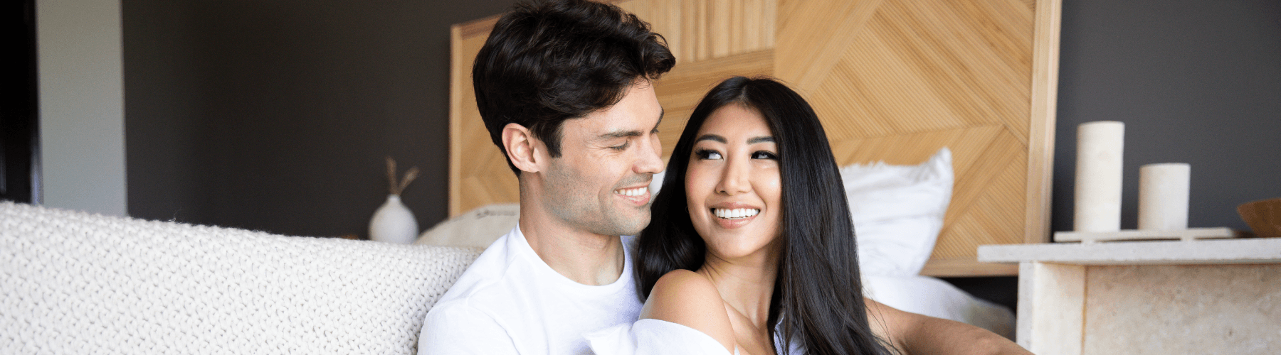 Smiling couple relaxing on bed in modern, cozy bedroom, promoting JIMMYJANE luxury lifestyle