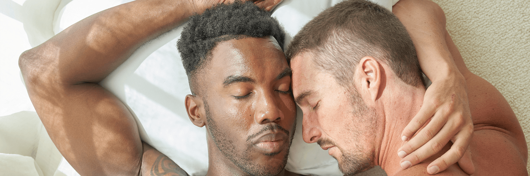 Interracial couple lying together in bed, embracing, natural morning light, JIMMYJANE lifestyle