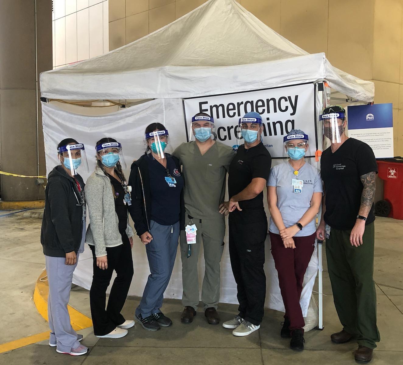 Healthcare workers in face shields and masks at emergency screening tent