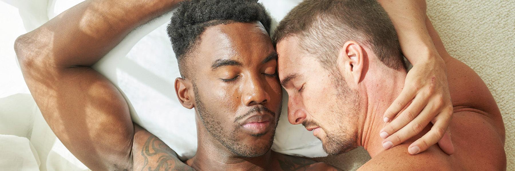 Two men embracing and relaxing closely on a bed in soft natural light, intimacy lifestyle