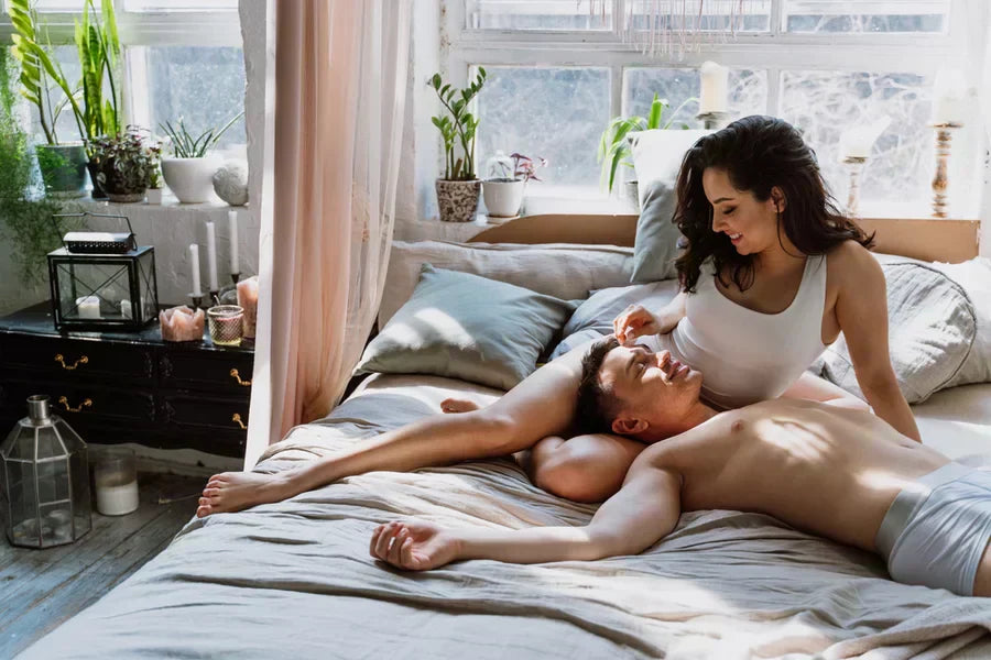 Young couple relaxing together on a sunlit bed in a cozy, modern bedroom with plants
