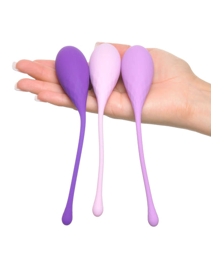 A hand holding three purple and pink silicone weights from the Fantasy® For Her Pipedream® Kegel Train-Her Set, each with long handles—ideal as a weighted kegel exerciser.