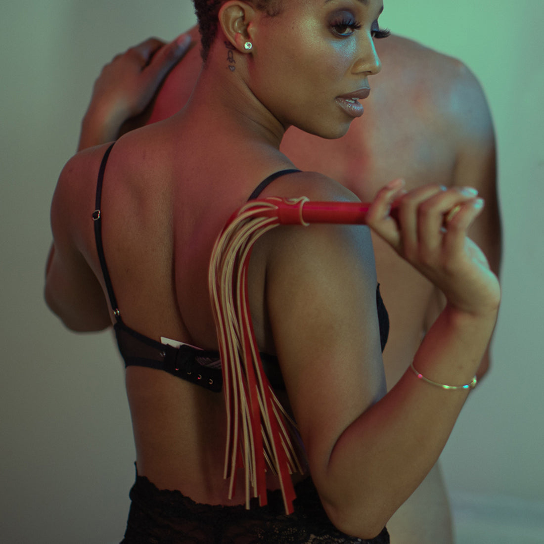 Woman holding vegan leather bondage whip behind her back