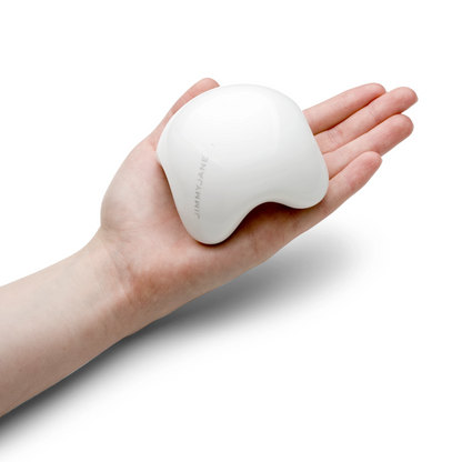 A hand holds the JIMMYJANE® Contour White Ceramic Massage Stone against a white background, highlighting its smooth, ergonomic design perfect for a luxurious full-body massage.