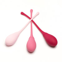 Self + Jimmyjane small, medium, and large kegel trainers set in light pink, pink, and burgundy laying on table