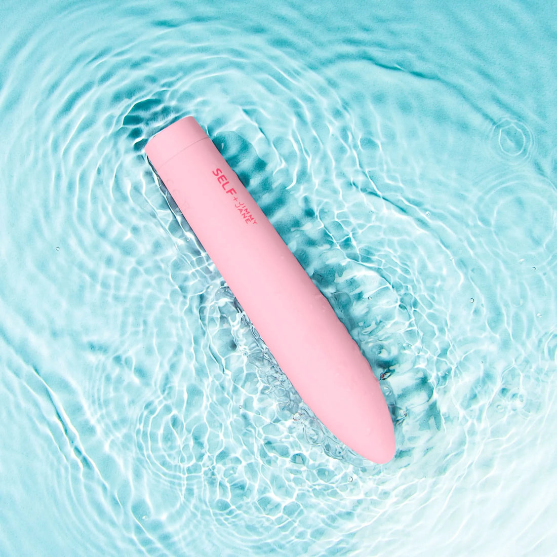 Self + Jimmyjane vibrating slimline massager in light pink laying in rippling water